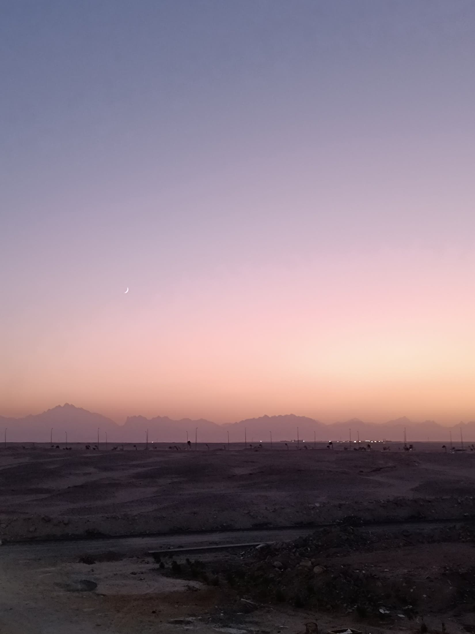 A crescent moon over the dunes at dusk.
