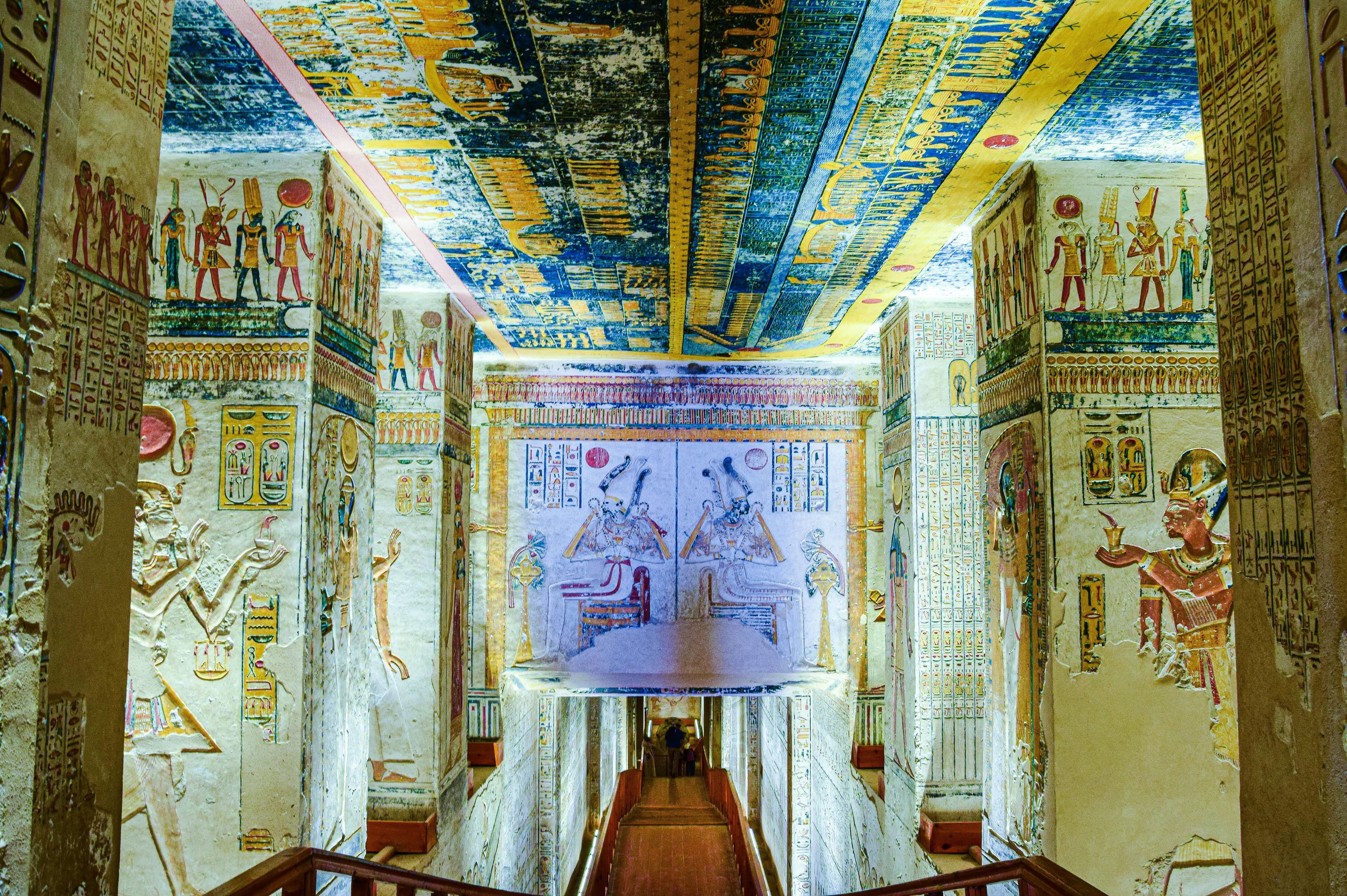 A tomb ceiling of deities above a descending stair.